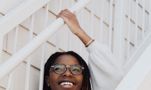 Girl with glasses in white sitting on white stairs smiling