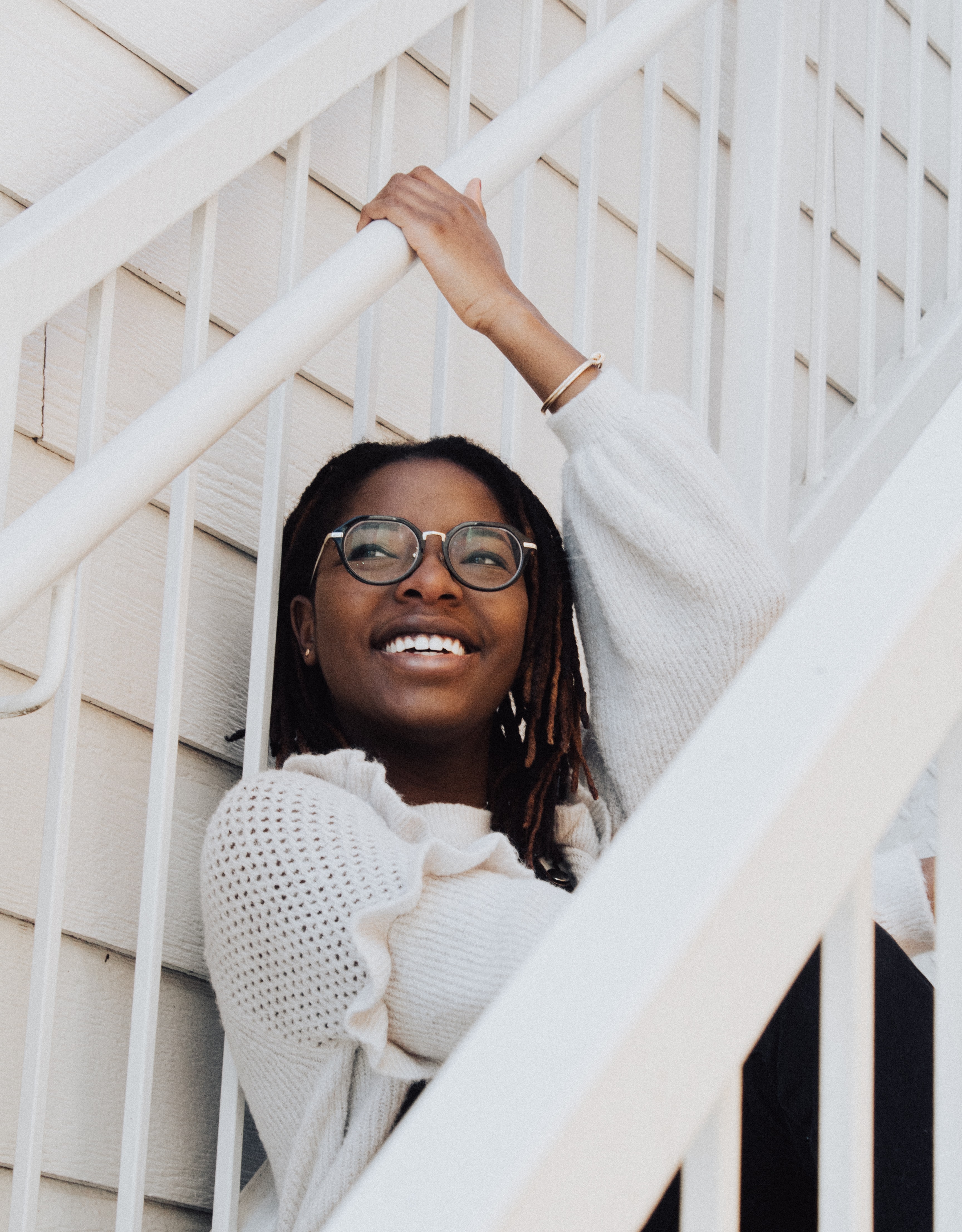 Girl with glasses in white sitting on white stairs smiling